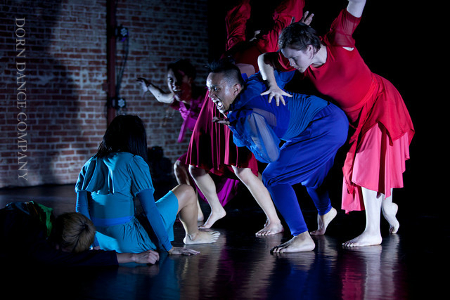 Dancers from @blaktinxdance huddled together on stage wearing jewel toned costumes.