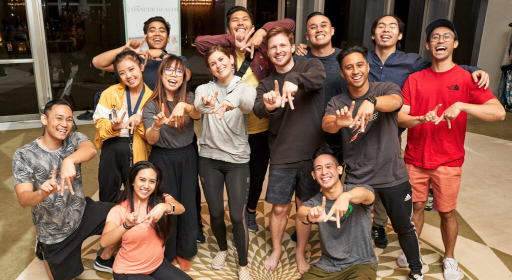 Dance Resource Center Day of Dancer Health diverse group of happy dancers making LA sign with hands.