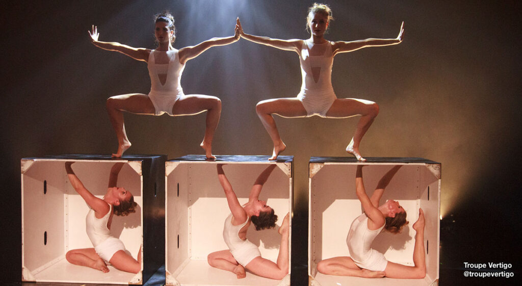 Dancers from @troupevertigo company on stage, three in boxes and two above in plie second position forced arch.